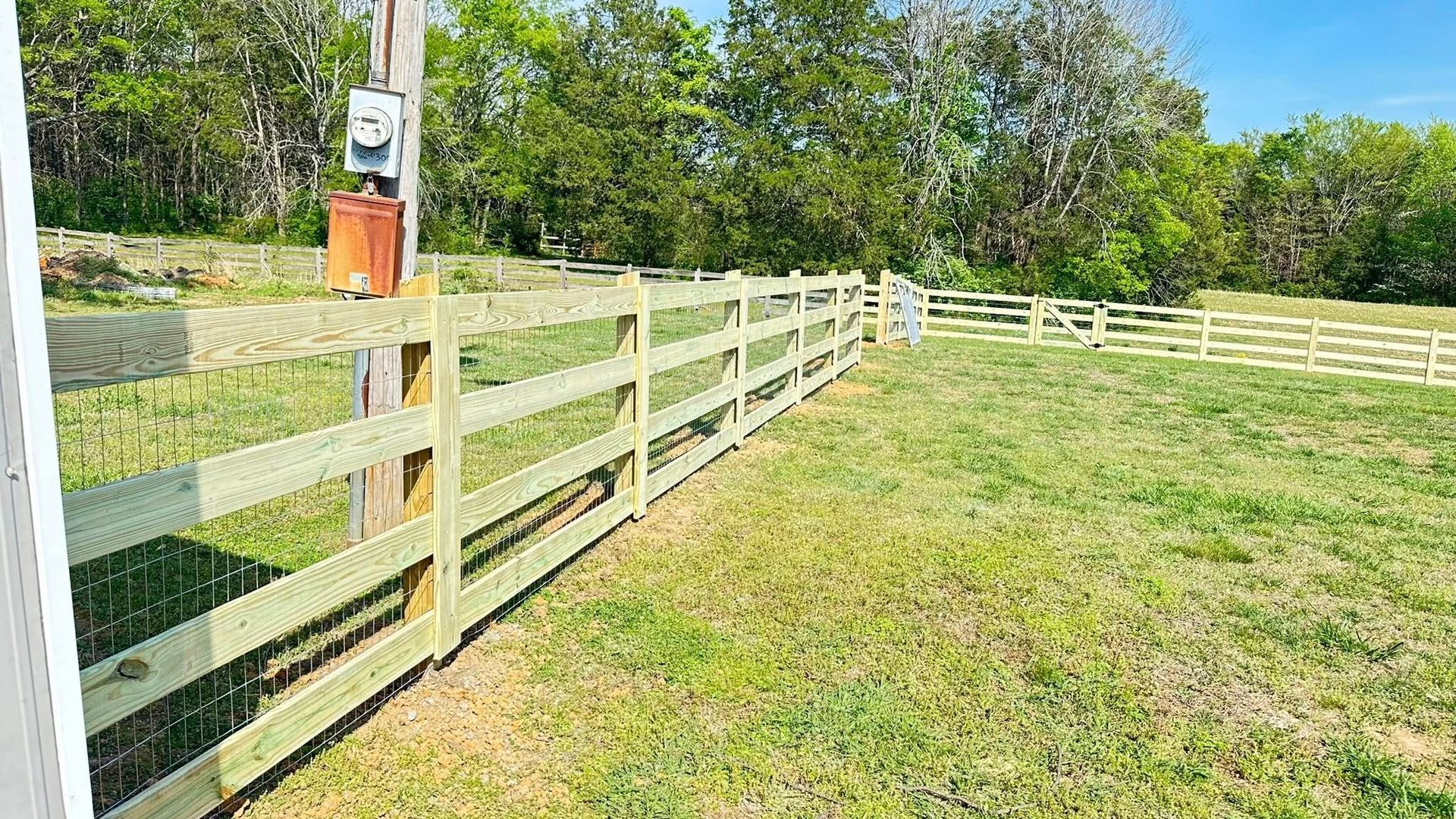 White wooden fence along a grassy yard with trees in the background