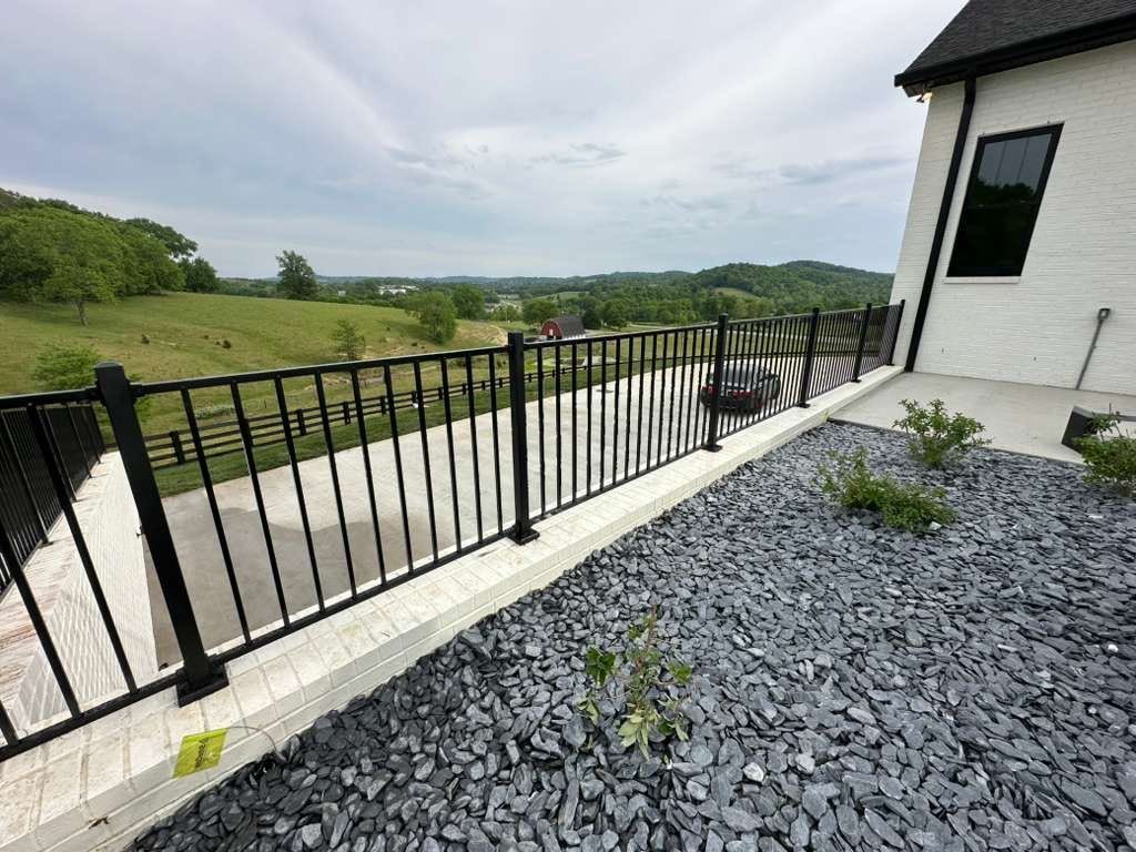 Black metal railing on a patio overlooking a grassy hillside and cloudy sky