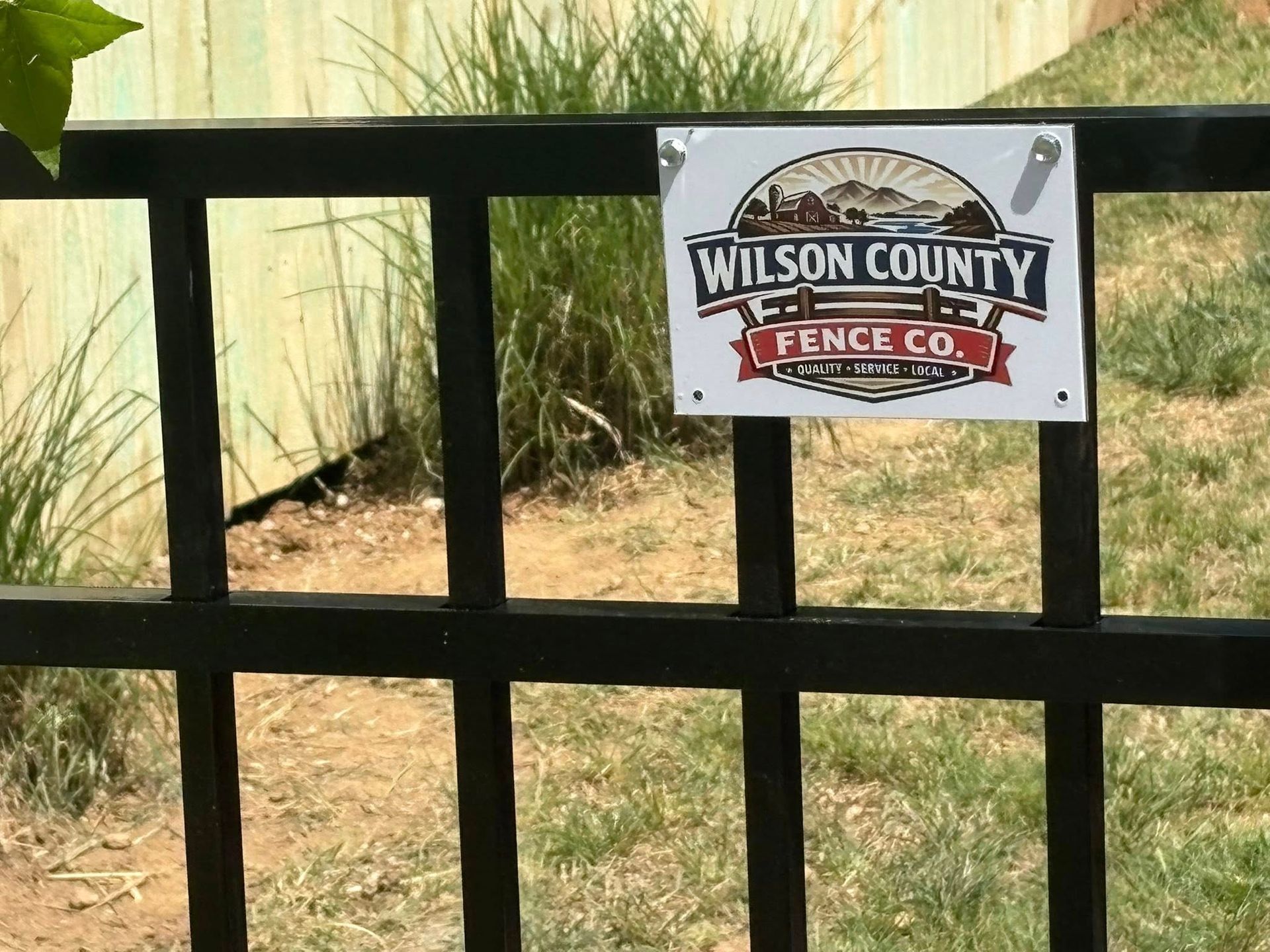 Black metal fence with a Wilson County Fence Co. sign in front of tan grasses