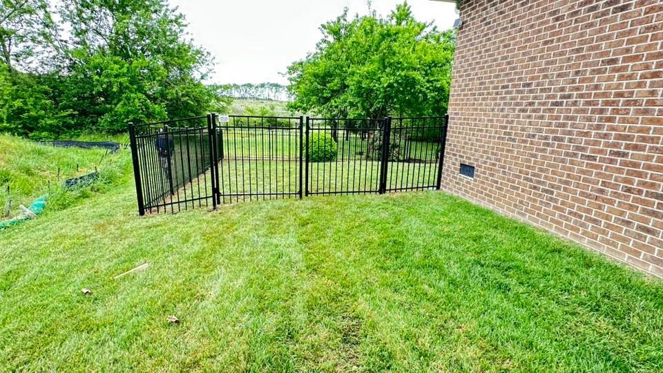Grassy backyard with a black metal gate and a brick house wall on the right