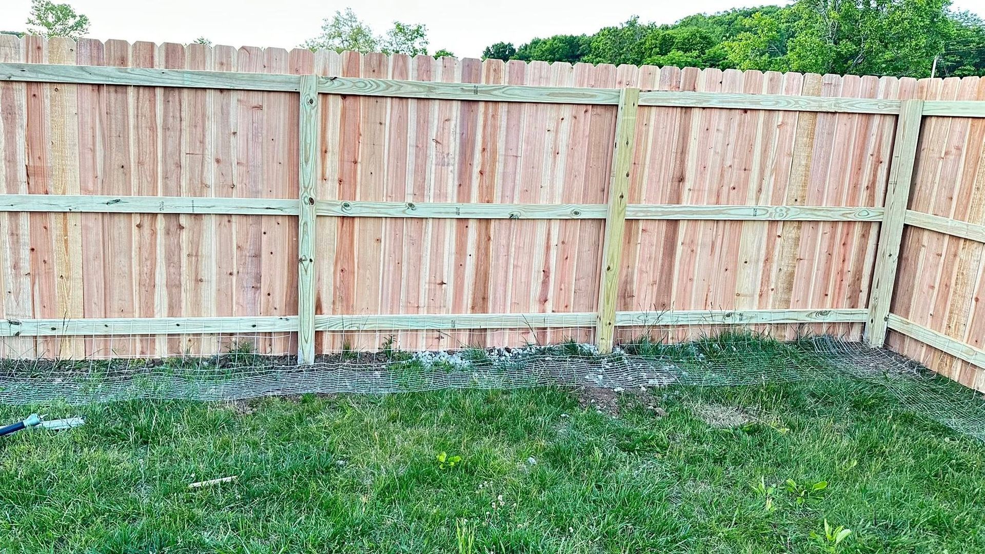 Wooden privacy fence along a grassy backyard under a cloudy sky.