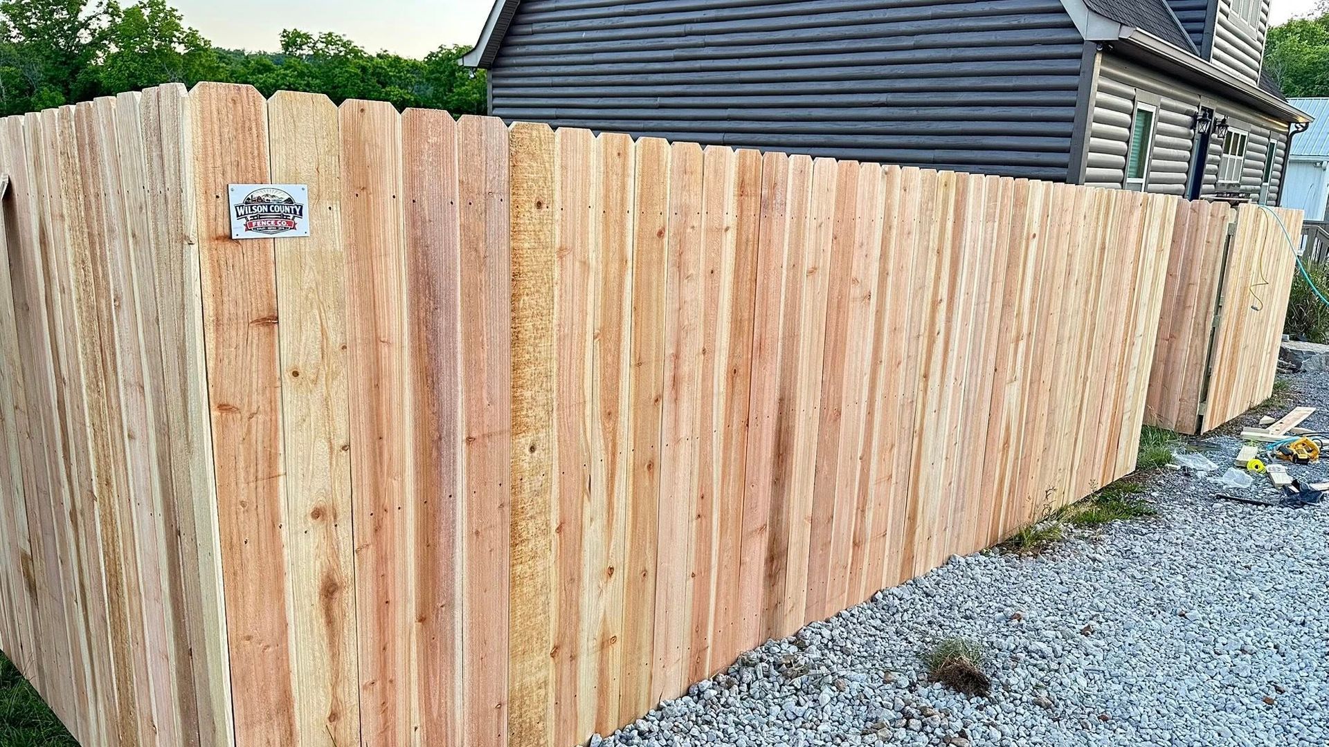 New wooden privacy fence along a gravel side yard beside a house