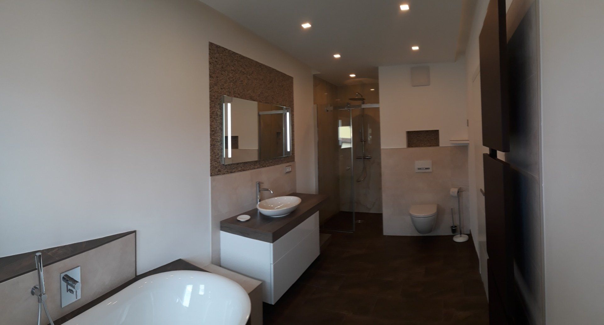 Modernes Badezimmer mit weißen Wänden, dunklem Holzboden, weißem Waschbecken und Dusche.