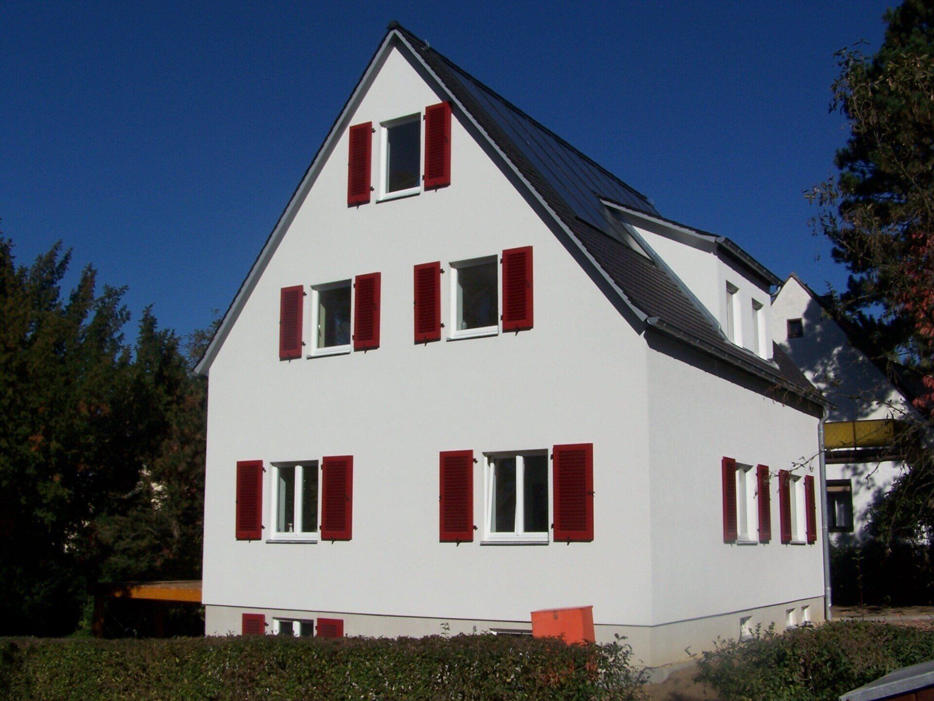Weißes Haus mit dunkelroten Fensterläden vor blauem Himmel.
