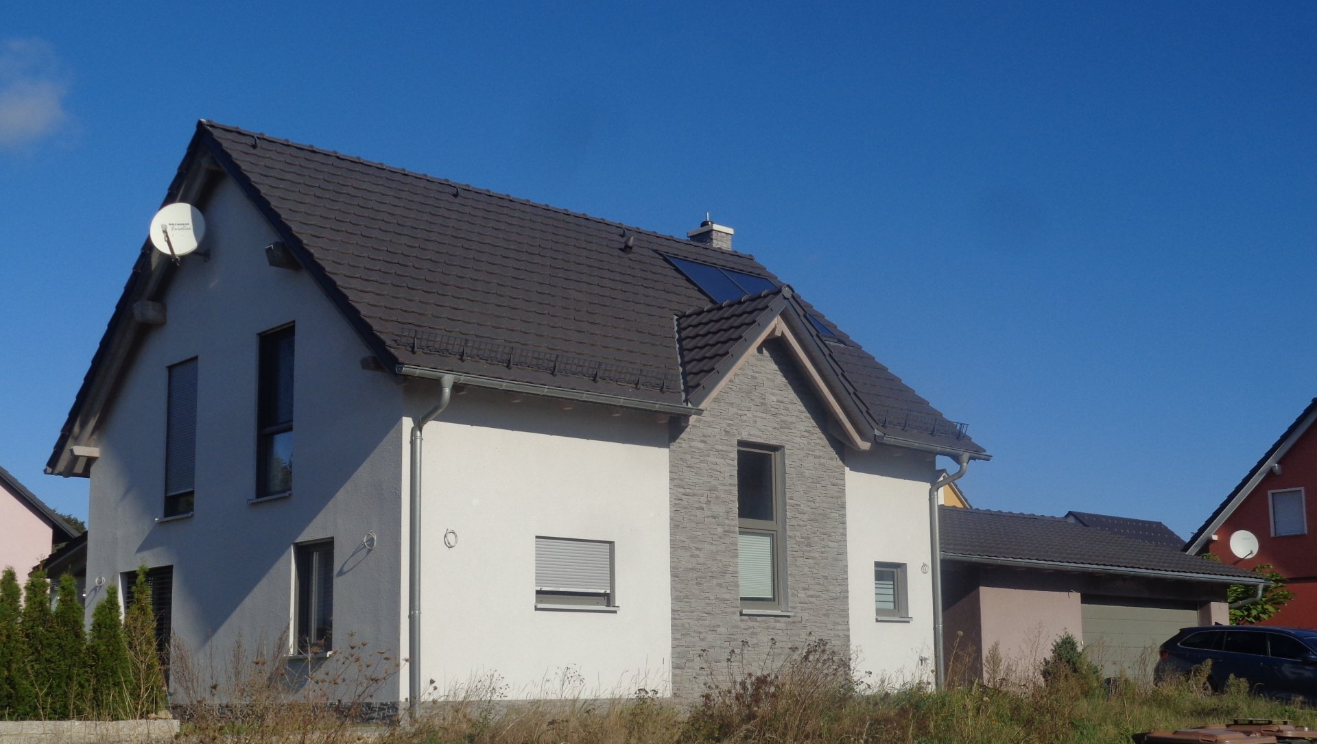 Zweistöckiges Haus mit grauem Dach, weiß-grauer Fassade, blauem Himmel und einer Satellitenschüssel.