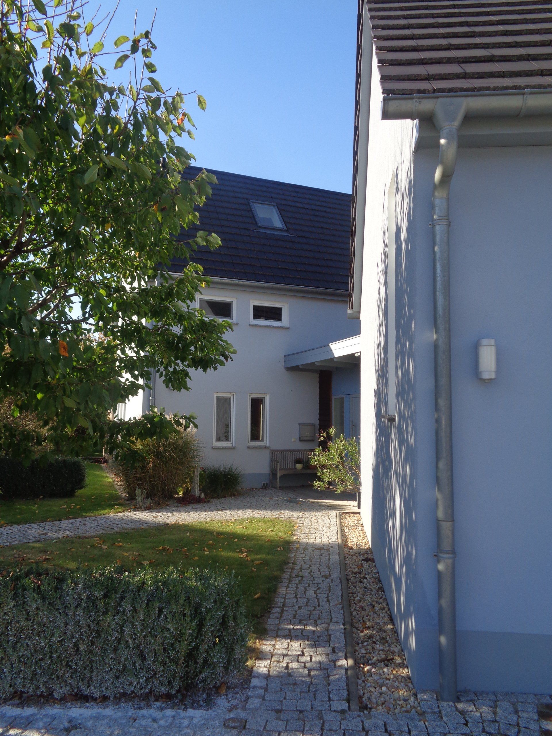 Zweistöckiges hellblaues Gebäude mit einem Weg und einem Baum; blauer Himmel im Hintergrund.