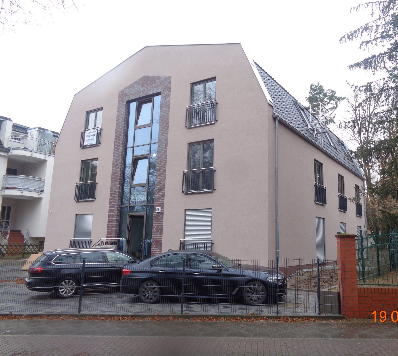 Modernes beiges Mehrfamilienhaus mit Glaseingang, Balkonen und zwei Parkplätzen.