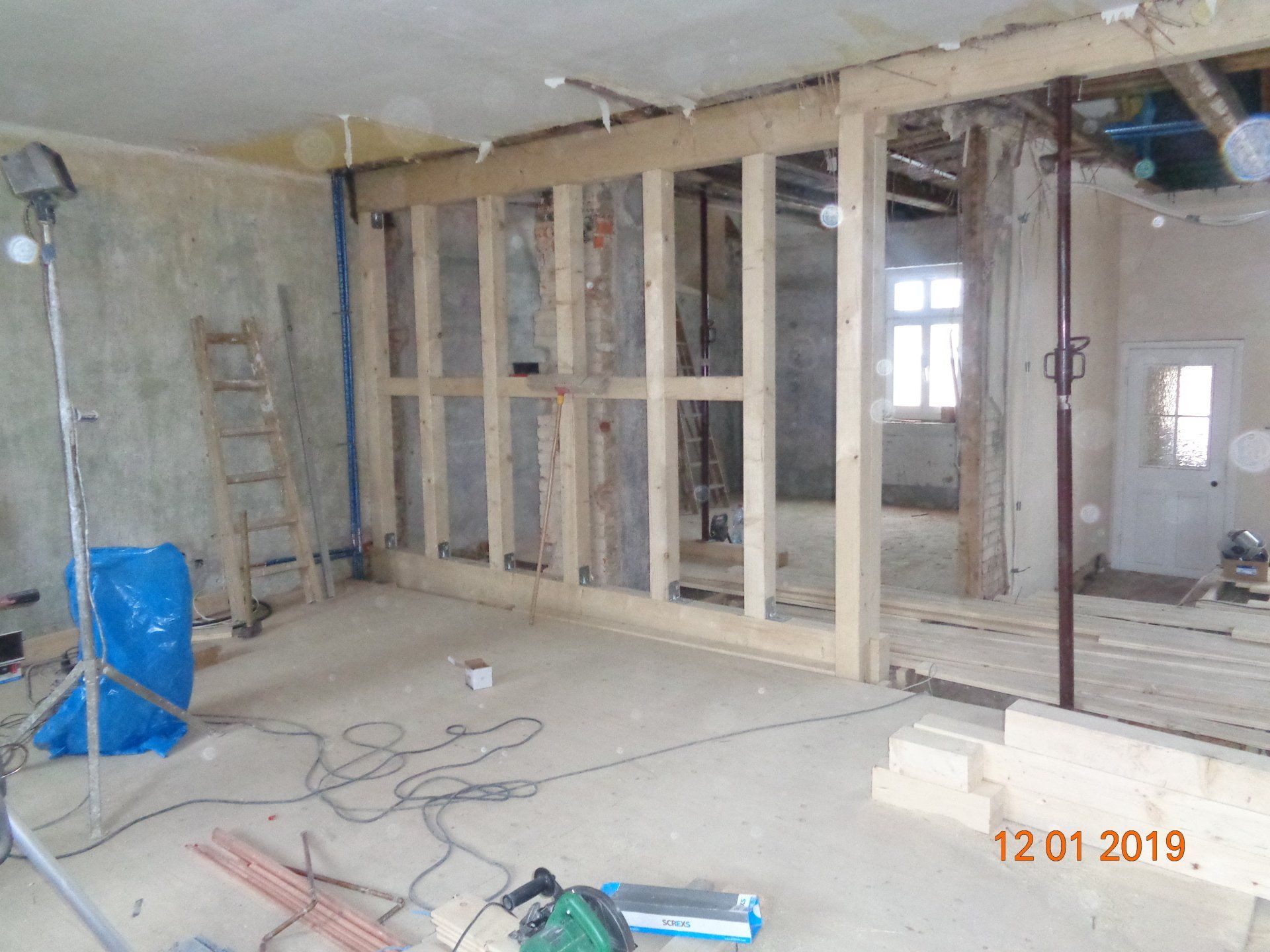 Innenansicht einer Baustelle mit Holzrahmenwänden, Werkzeugen und freiliegenden Balken.