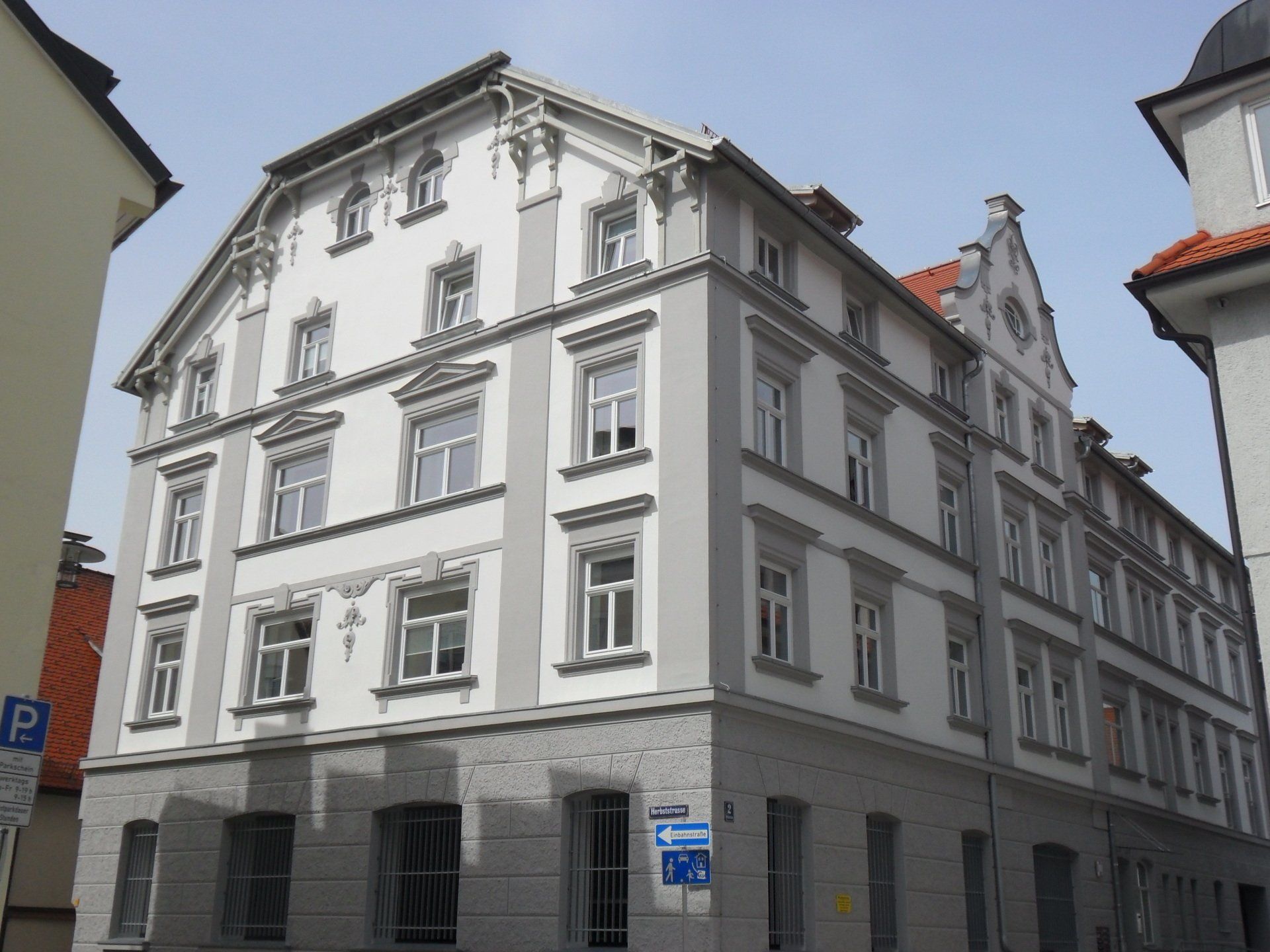 Grau-weißes mehrstöckiges Gebäude mit mehreren Fenstern; Straßenschilder sichtbar.