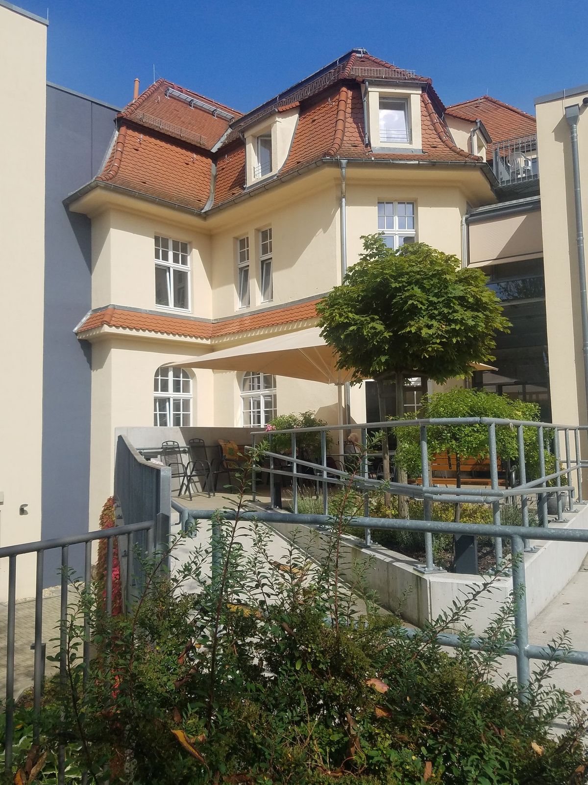 Beiges Gebäude mit rotem Ziegeldach, kleinem Innenhof und Grünanlagen.