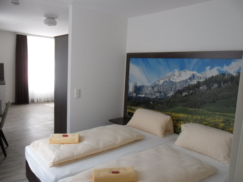 Schlafzimmer mit zwei Betten, einem Kopfteil mit Bergmotiv und einer offenen Tür zu einem anderen Zimmer.