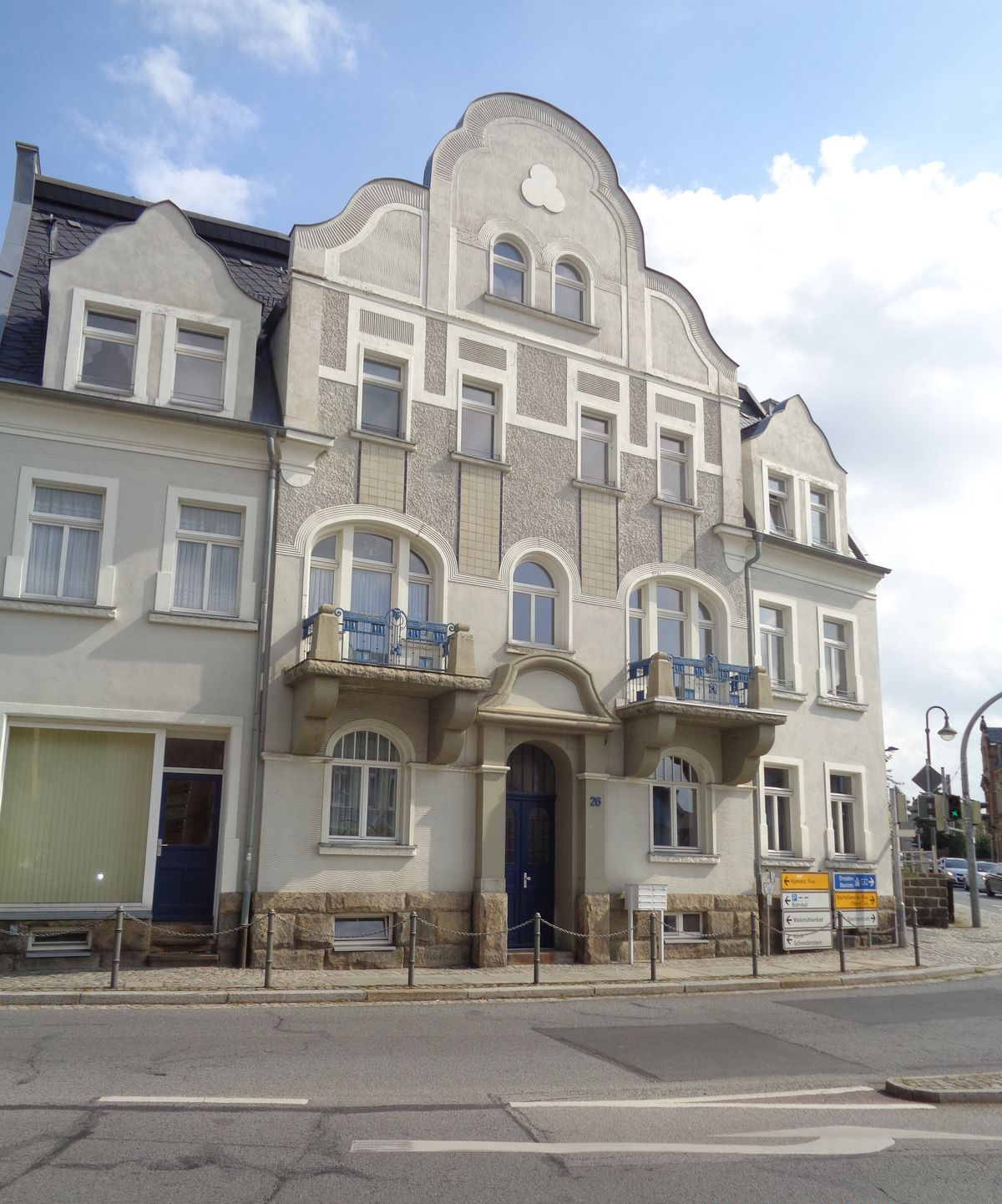 Graues mehrstöckiges Gebäude an einer Straßenecke mit Bogenbalkonen und einem markanten zentralen Giebel.