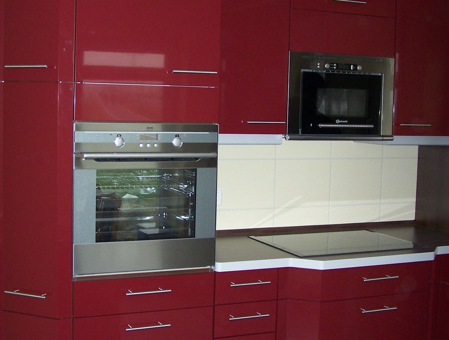 Rote Küchenschränke mit eingebautem Backofen und Mikrowelle. Küchengeräte aus Edelstahl.