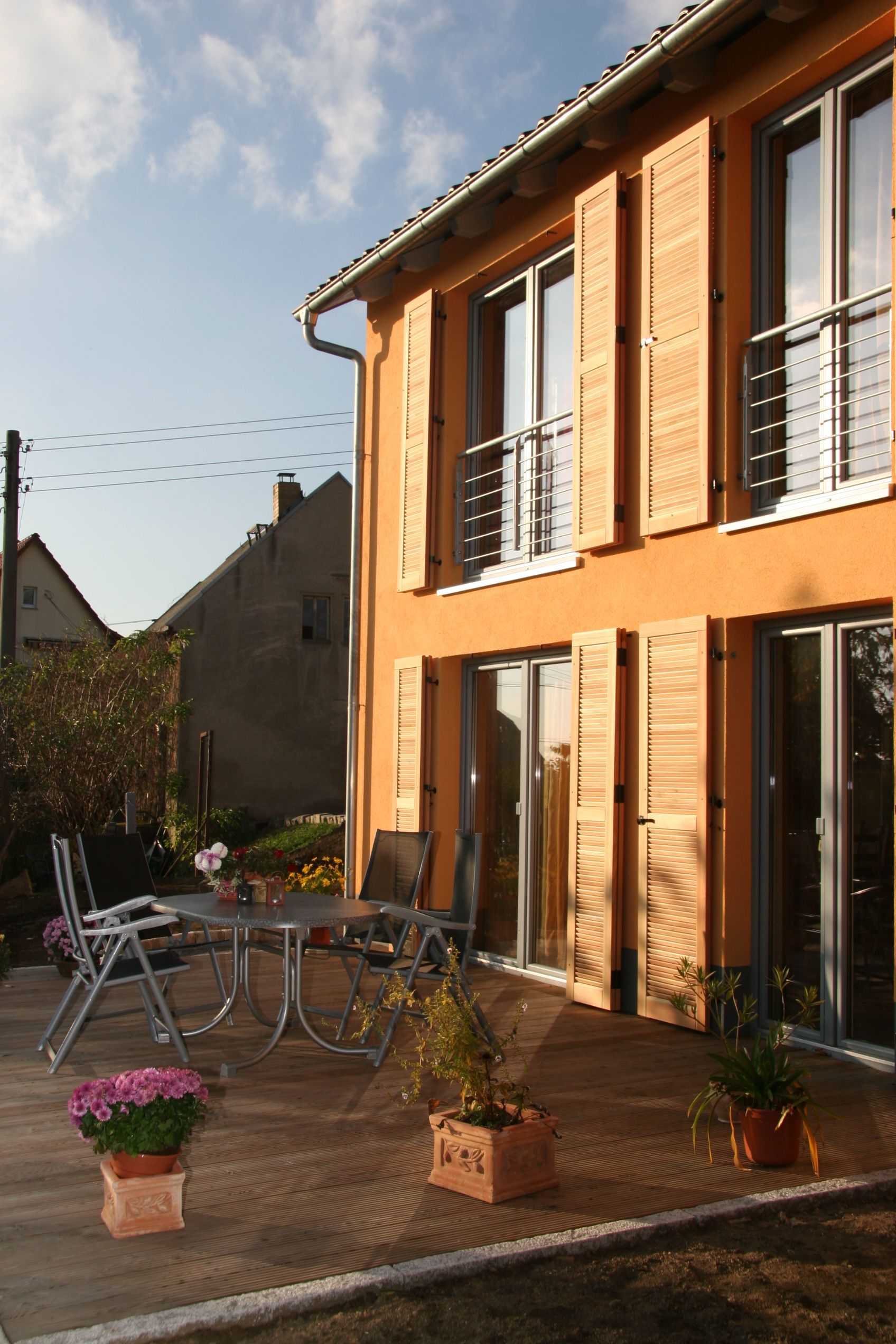 Orangefarbenes Haus mit Holzfensterläden, Sitzgelegenheiten im Freien und Topfpflanzen auf einer Terrasse.