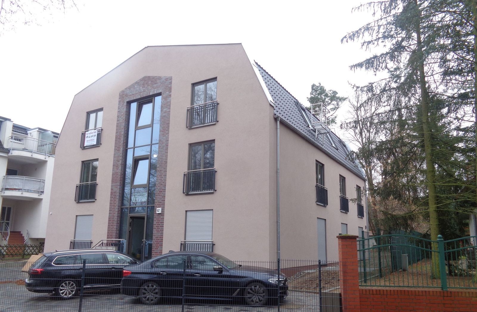 Beiges Gebäude mit großem Glaseingang, davor parken schwarze Autos.