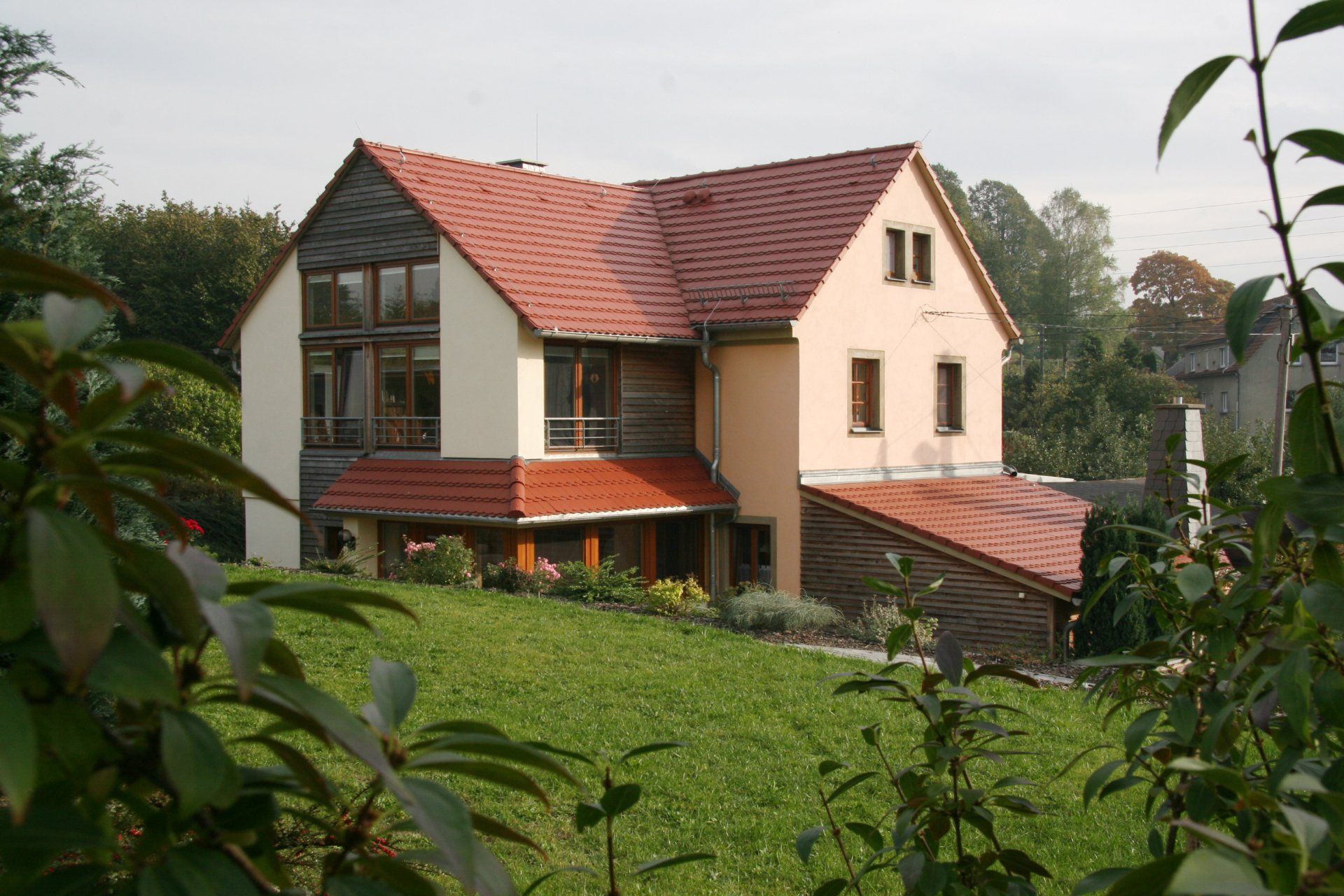 Beiges Haus mit rotem Dach, Holzelementen und großen Fenstern auf einem grasbewachsenen Hügel.
