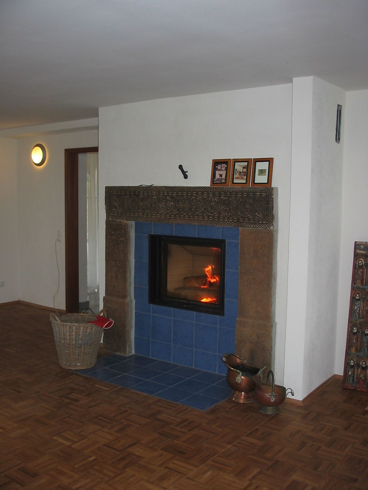 Kamin mit blauen Fliesen, brennendem Feuer und dekorativem Kaminsims in einem Raum mit Holzboden.