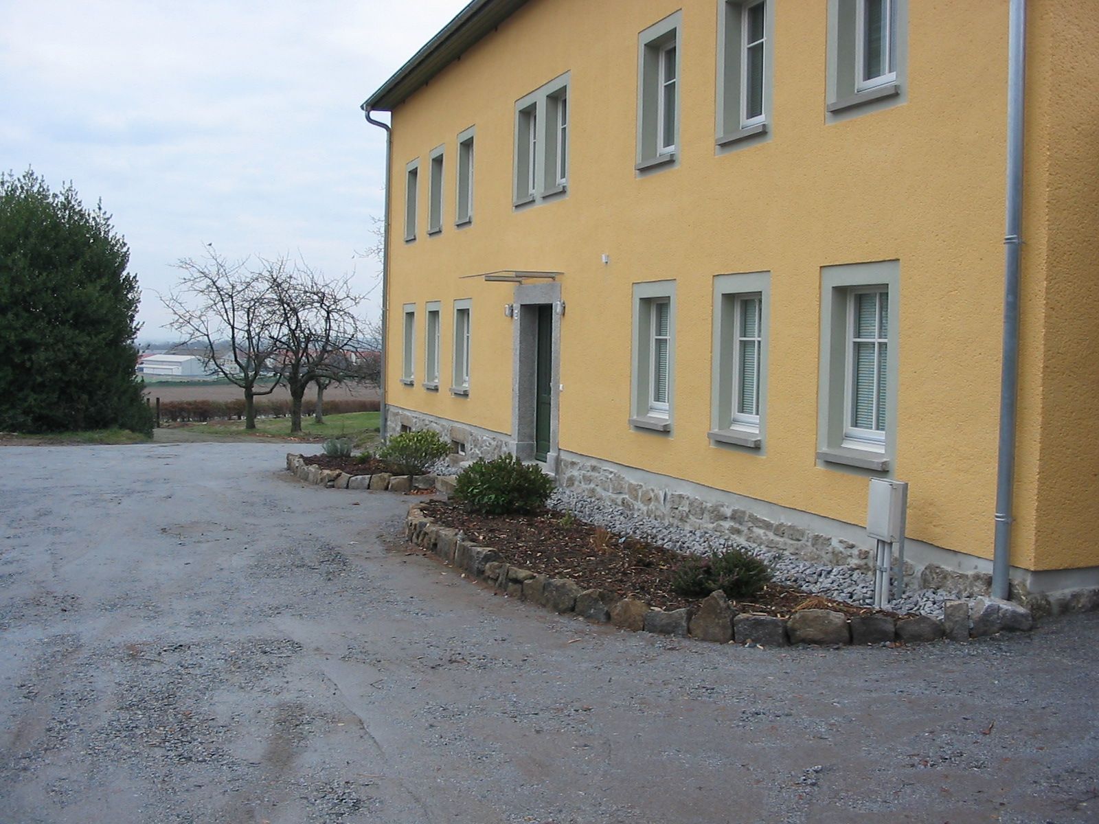 Gelbes Gebäude mit mehreren Fenstern und einer Kiesauffahrt.