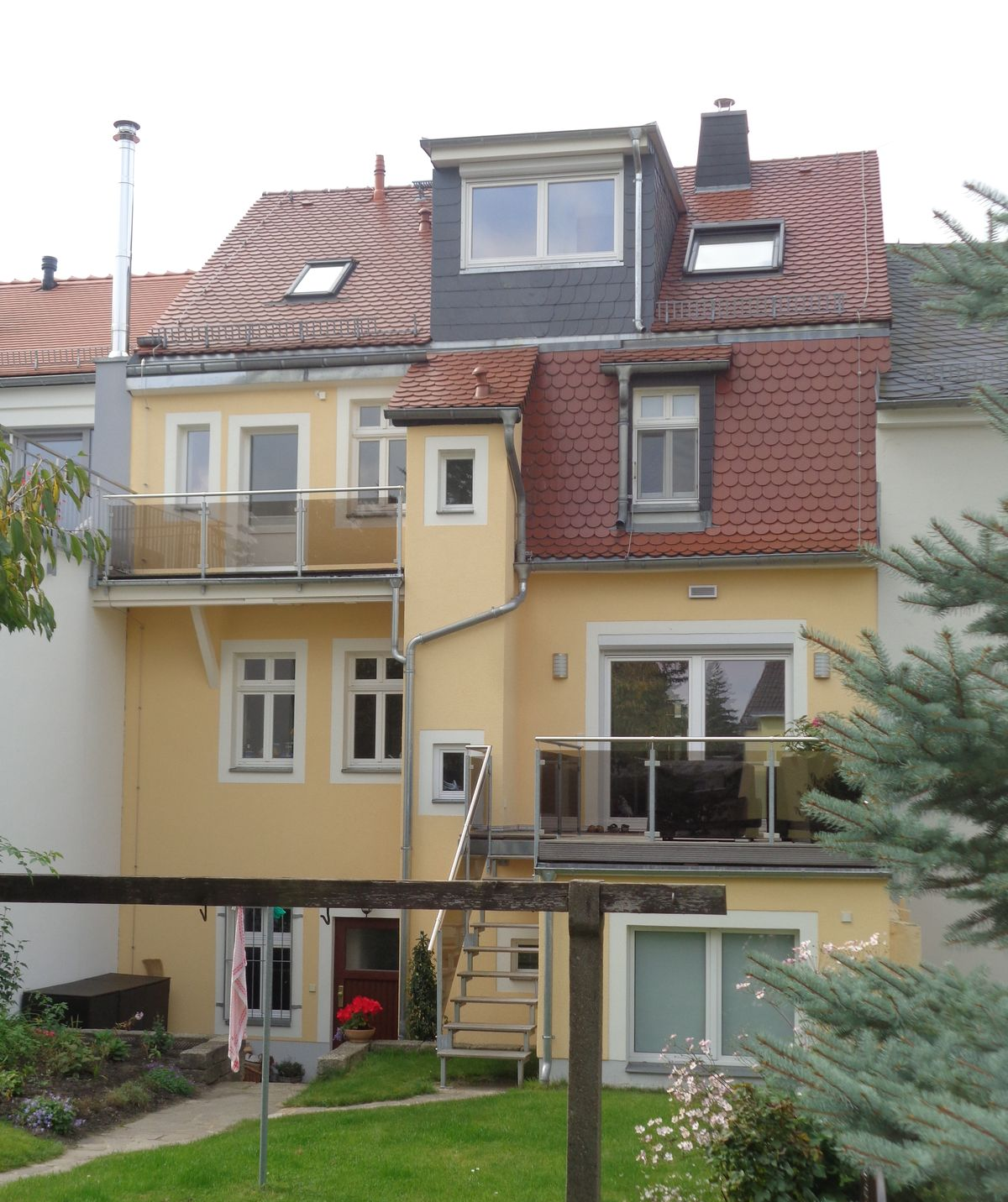 Gelbes Gebäude mit rotem Dach, mehreren Fenstern, Balkonen und einem kleinen Hof.