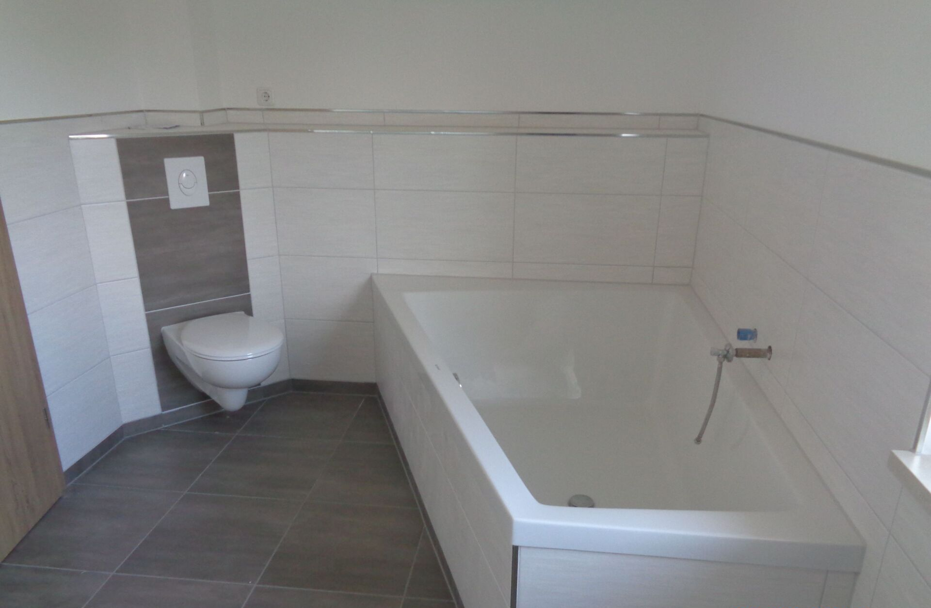 Badezimmer mit weißer Badewanne, Toilette sowie gefliesten Wänden und Boden.