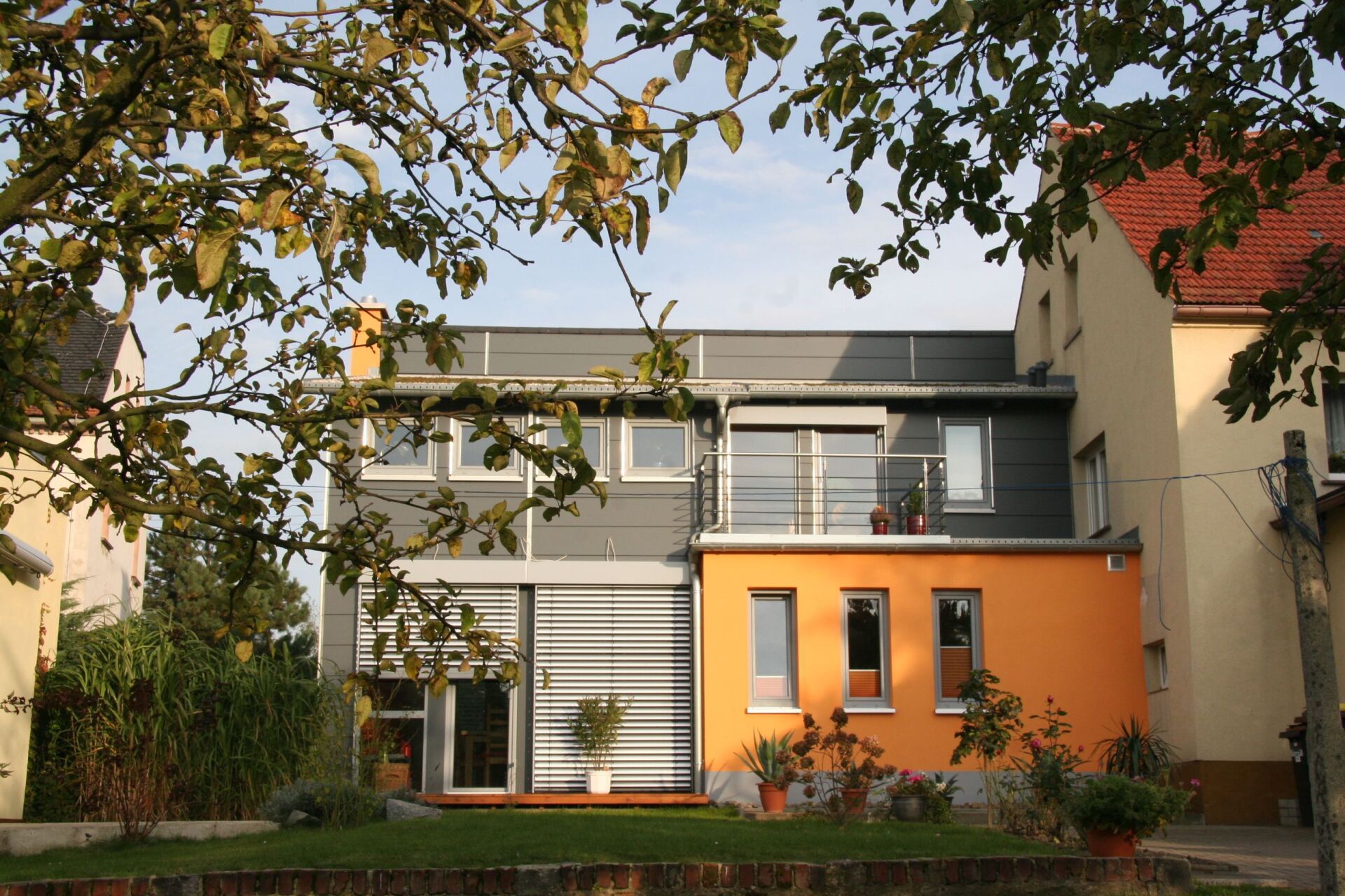 Modernes Gebäude mit orange-grauer Fassade, Balkon und Bäumen.