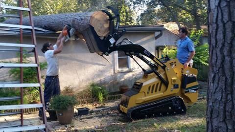 Construction workers using a yellow mini skid steer to lift a ladder beside a house