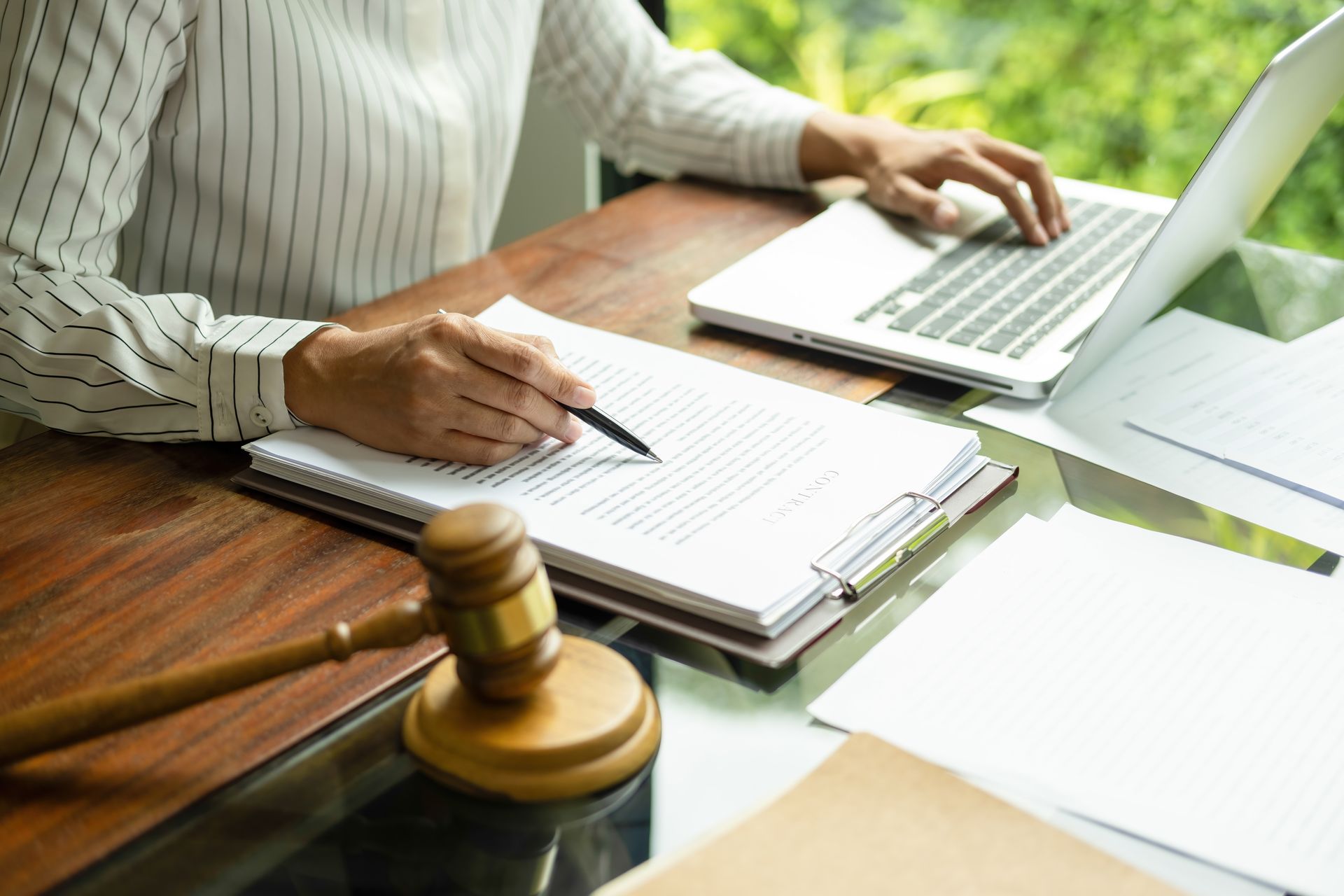 Person writing in a notebook beside a laptop and gavel on a wooden desk, suggesting legal work