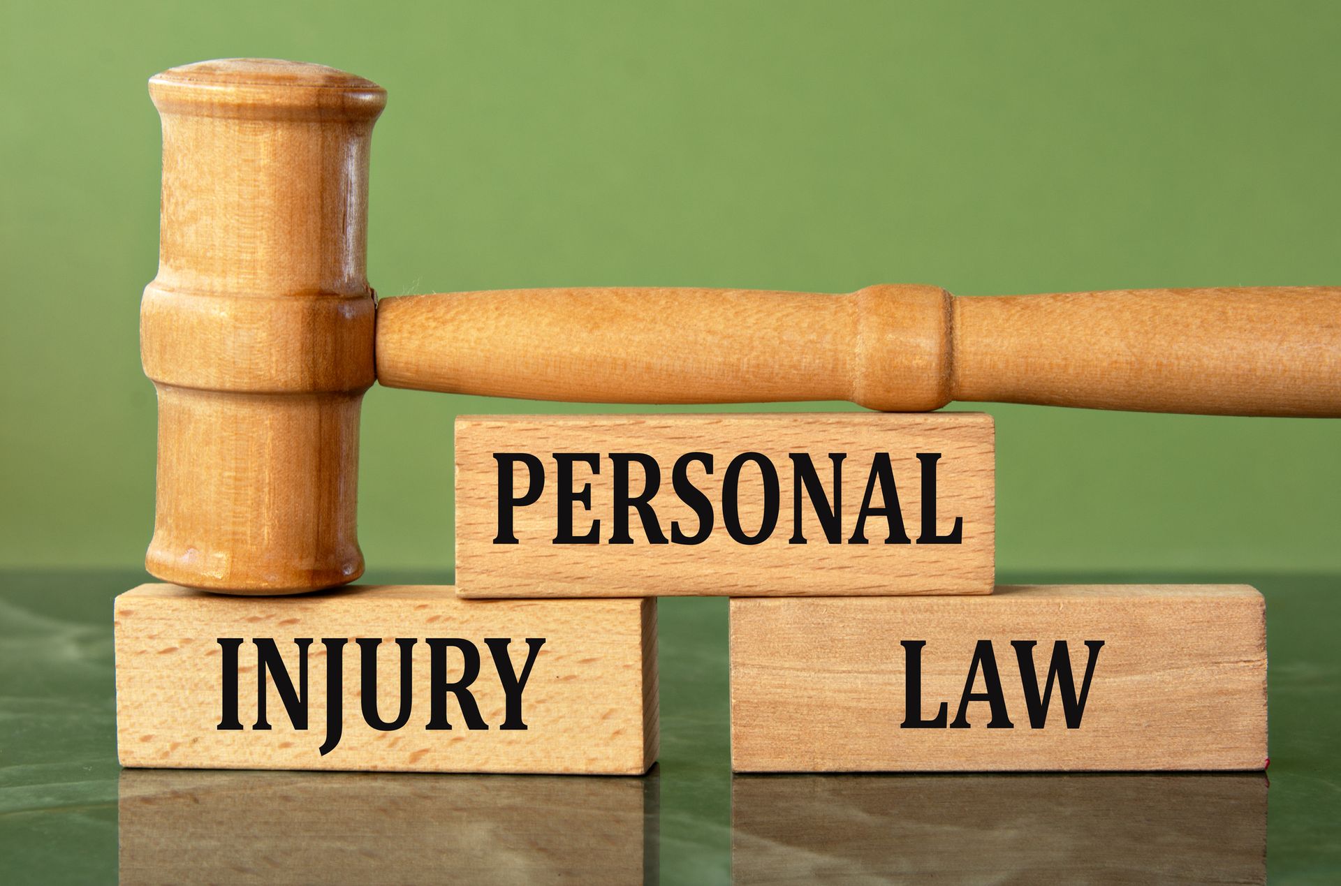 Wooden gavel atop blocks labeled 'Personal Injury Law' against a green background.