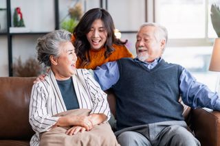 Three smiling people relaxing on a couch in a bright living room