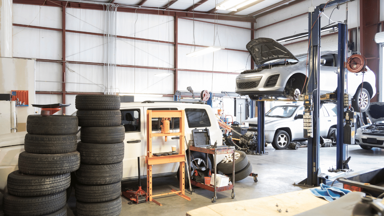 Car repair shop with cars on lifts, tires stacked, and tools.