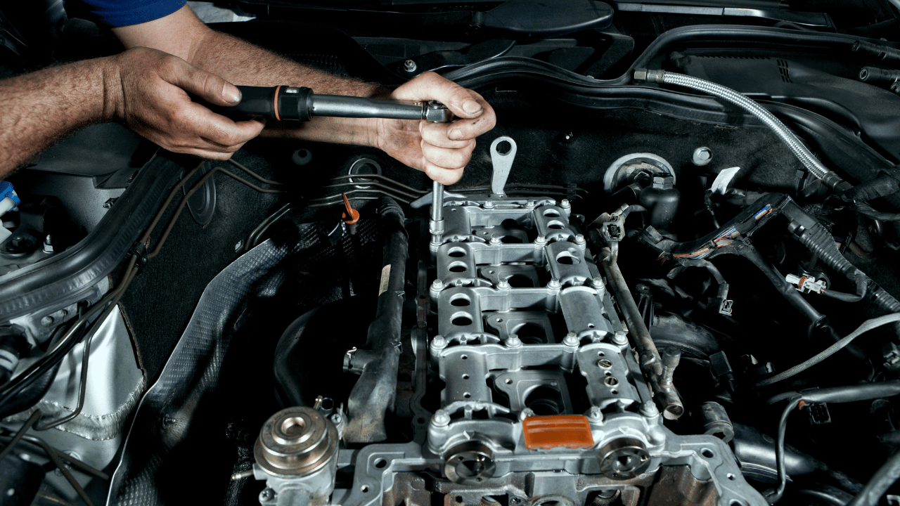 Hands using a tool to work on a car engine.
