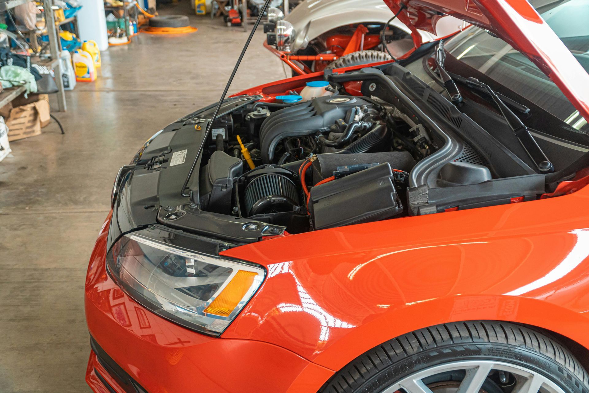 Bright orange car with hood open, engine visible in a garage setting.