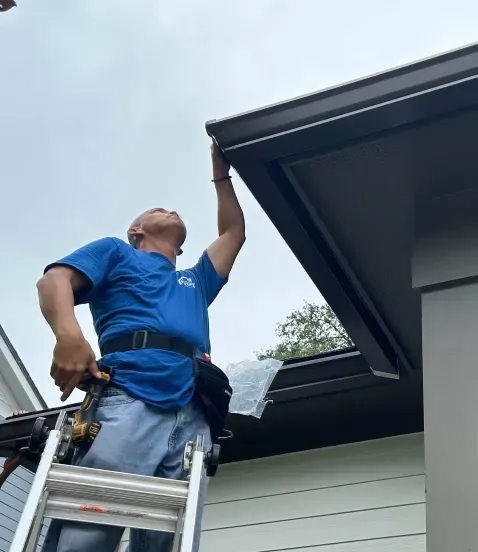 A man is standing on a ladder fixing a gutter on a house.