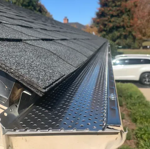 A close up of a gutter on a roof with a car parked in the background.