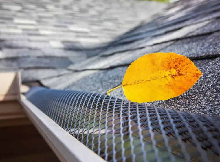 A yellow leaf is sitting on top of a gutter on a roof.
