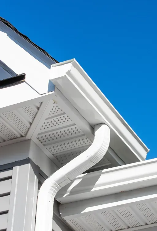 A white gutter on the side of a house with a blue sky in the background