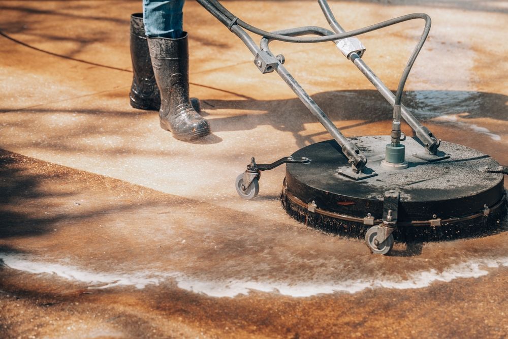 Pressure washing a concrete surface, with a worker’s boots and hose visible