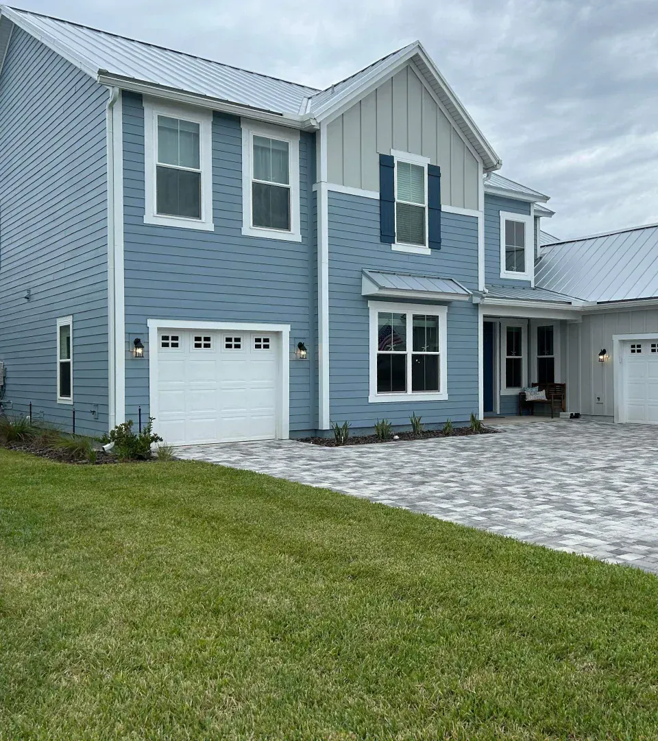 A large blue house with white trim and blue shutters is sitting on top of a lush green lawn.