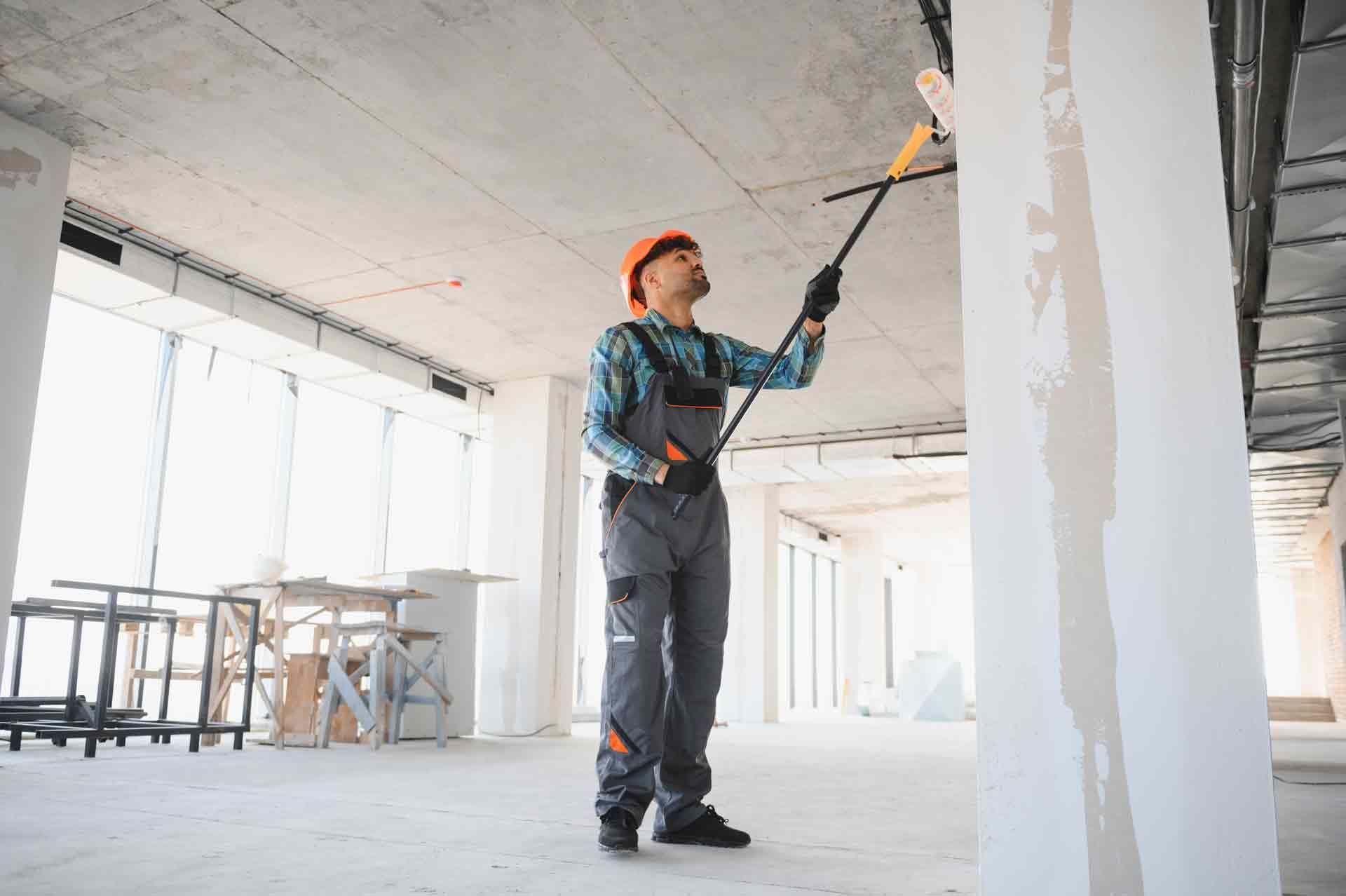 Construction worker painting walls and ceiling with telescopic paint roller.