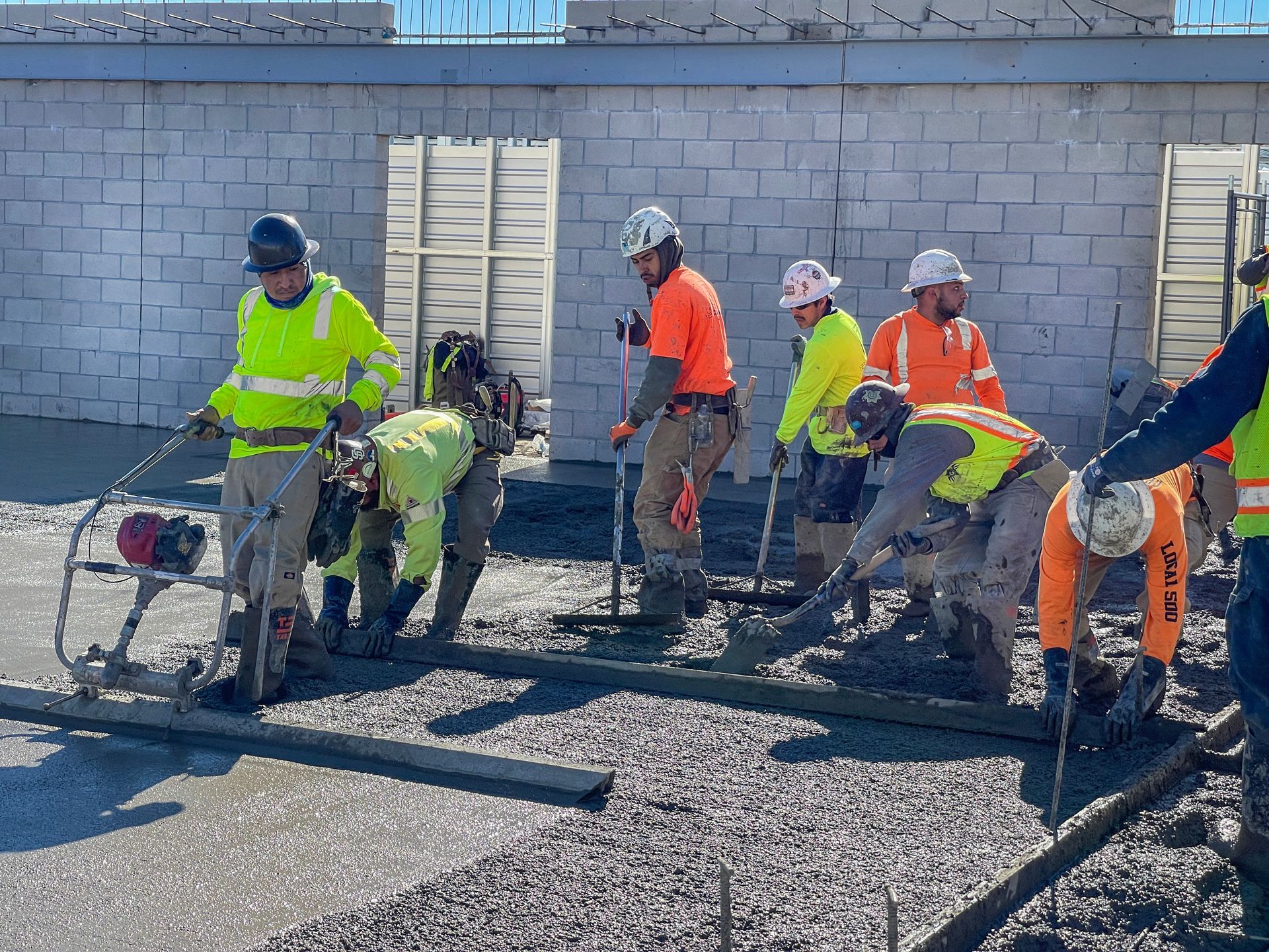 Construction crew pouring and leveling fresh concrete at a commercial job site.