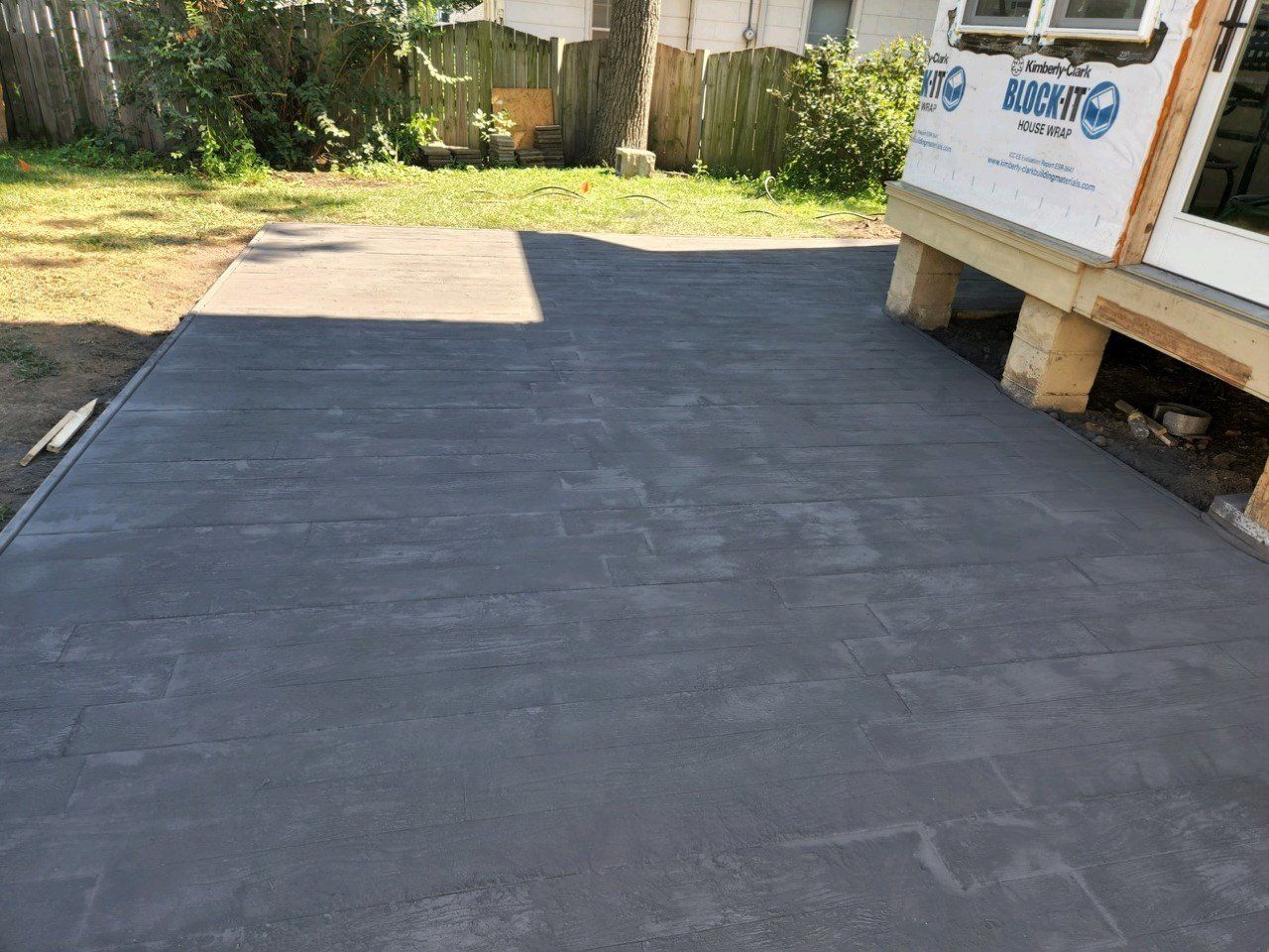 Freshly poured concrete patio next to a house under construction; gray, with construction materials visible.