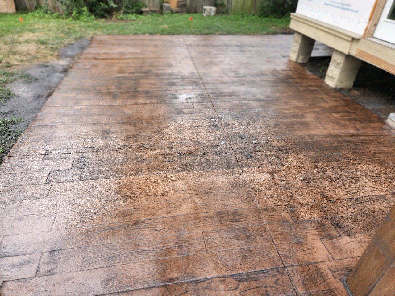 Stamped concrete patio, wood grain pattern, brown and dark gray hues, backyard setting.