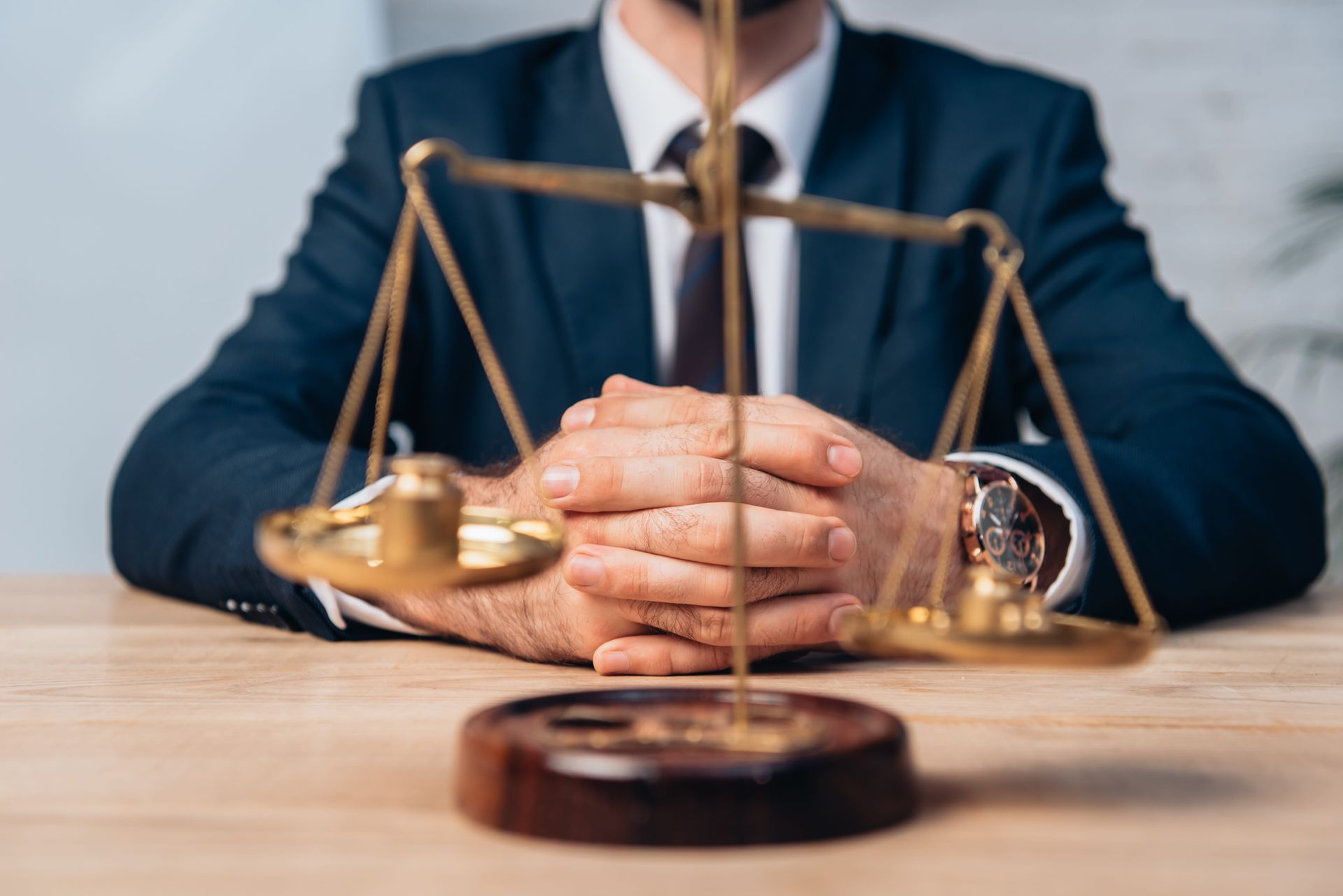 Lawyer in navy suit with clasped hands behind a brass scales of justice on a desk