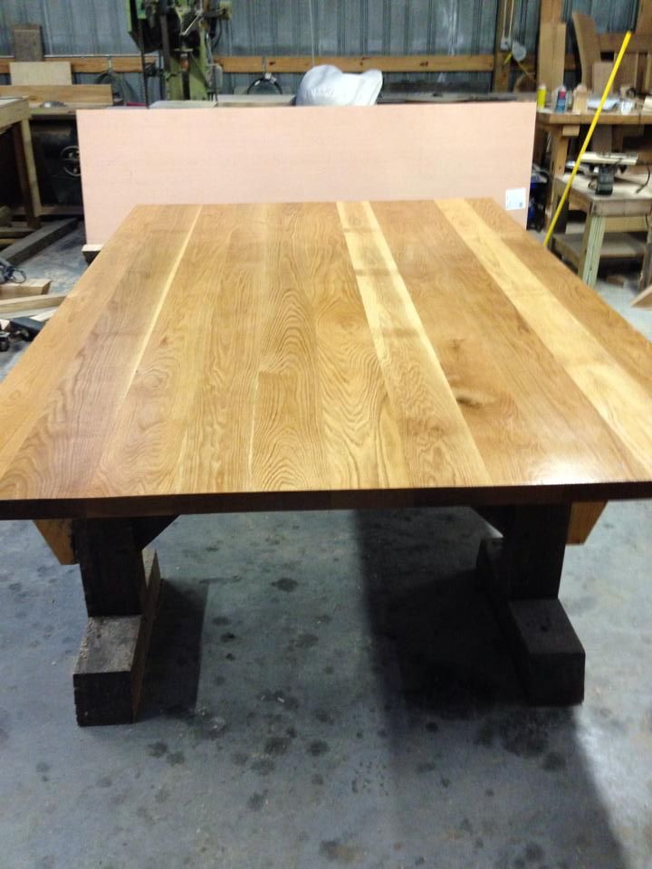 Wooden dining table on a workshop floor with thick block legs and a light wood top