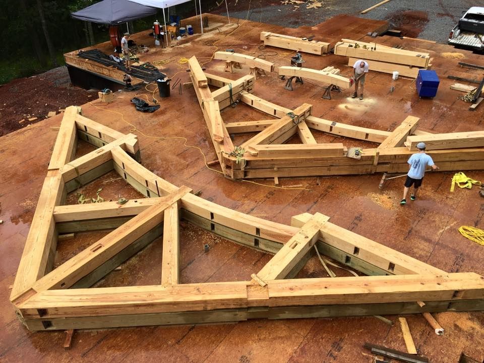 Wooden foundation framing laid out on a dirt lot, with a worker and construction materials nearby.