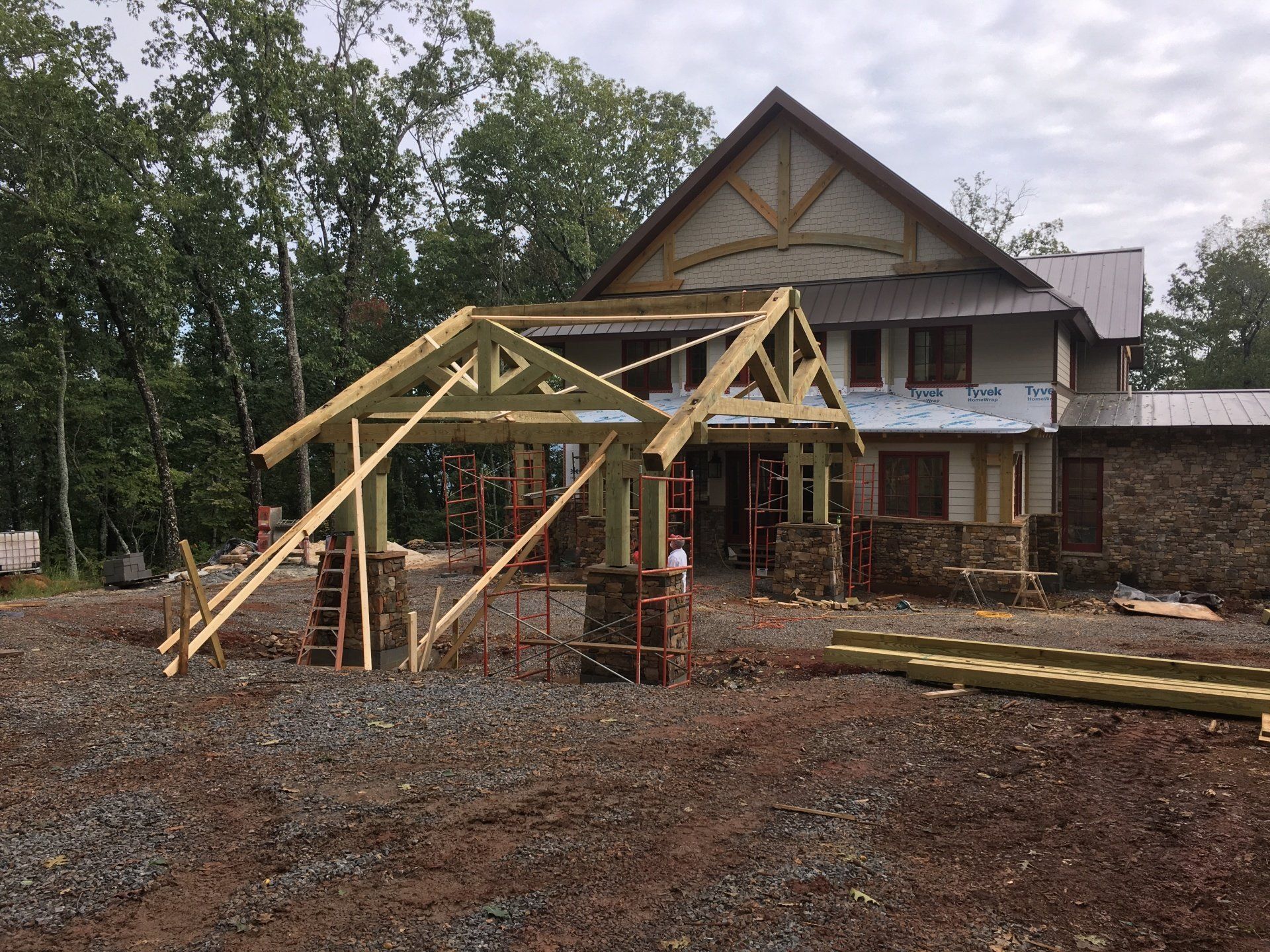 House under construction with wooden roof trusses and muddy yard in front of trees