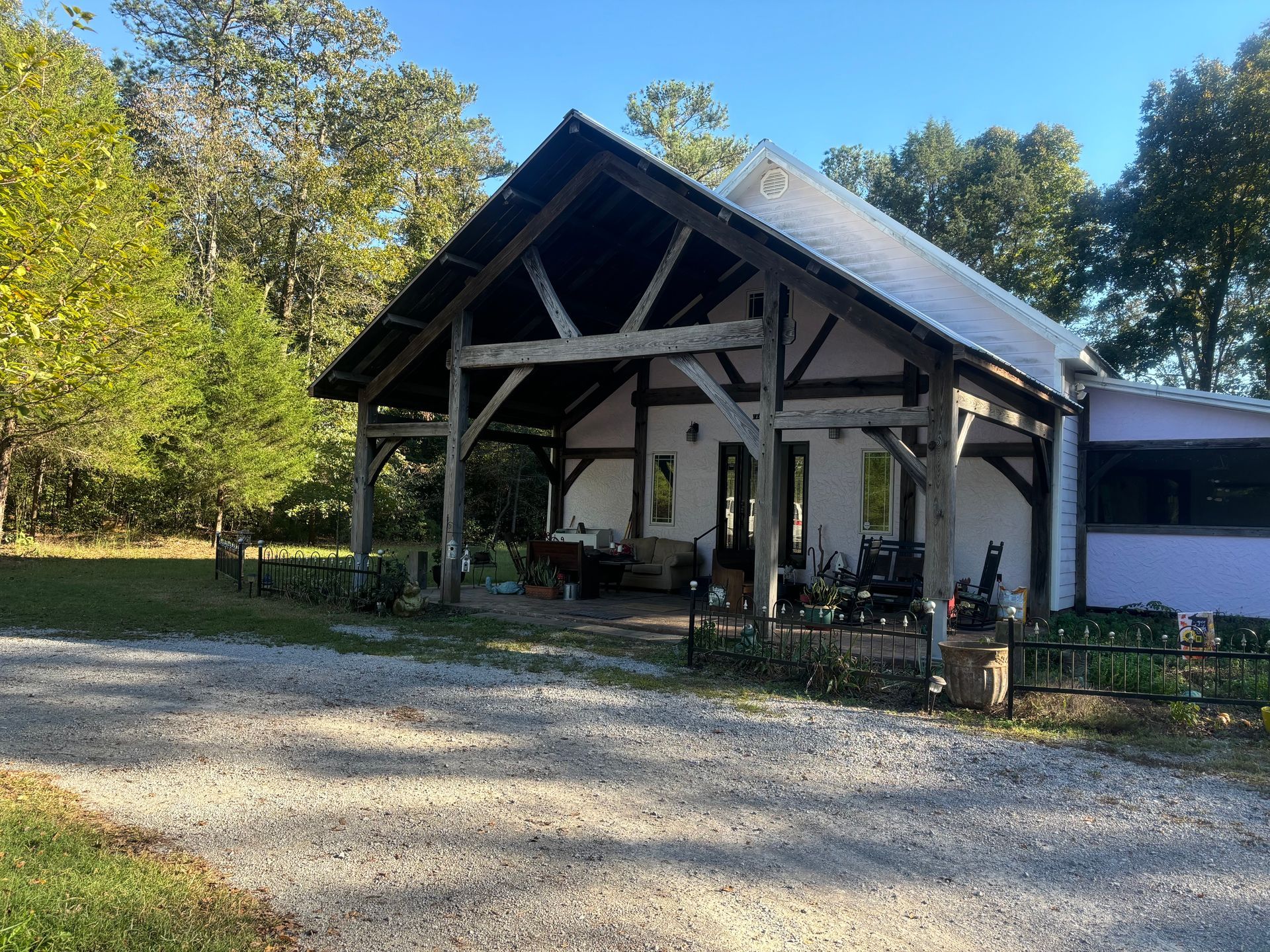 Gravel driveway leading to a white pavilion with a dark roof, surrounded by trees and greenery.
