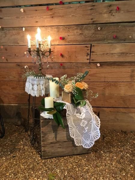 Decorative rustic display with candles, white lace, and flowers against a wooden wall