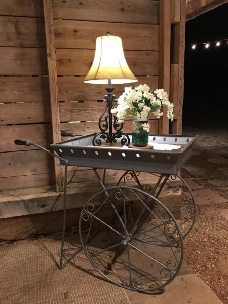 Rustic wagon wheel cart with a lit lamp and white flowers beside a wooden wall