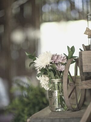 Glass jars of white and lavender flowers on a rustic wooden bench, with a blurred background